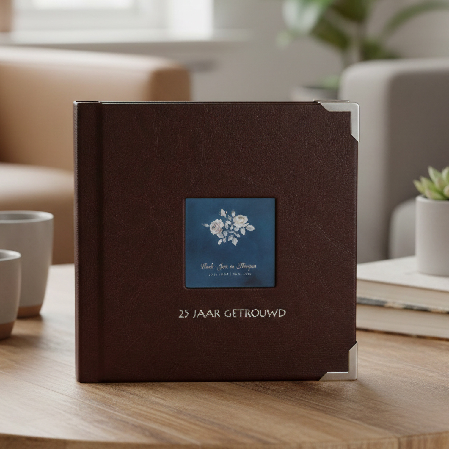 Bovenaanzicht van een vierkant bruin leren fotoboek op een houten koffietafel, met een venster op de cover waarin witte bloemen en de tekst '25 jaar getrouwd' te zien zijn.